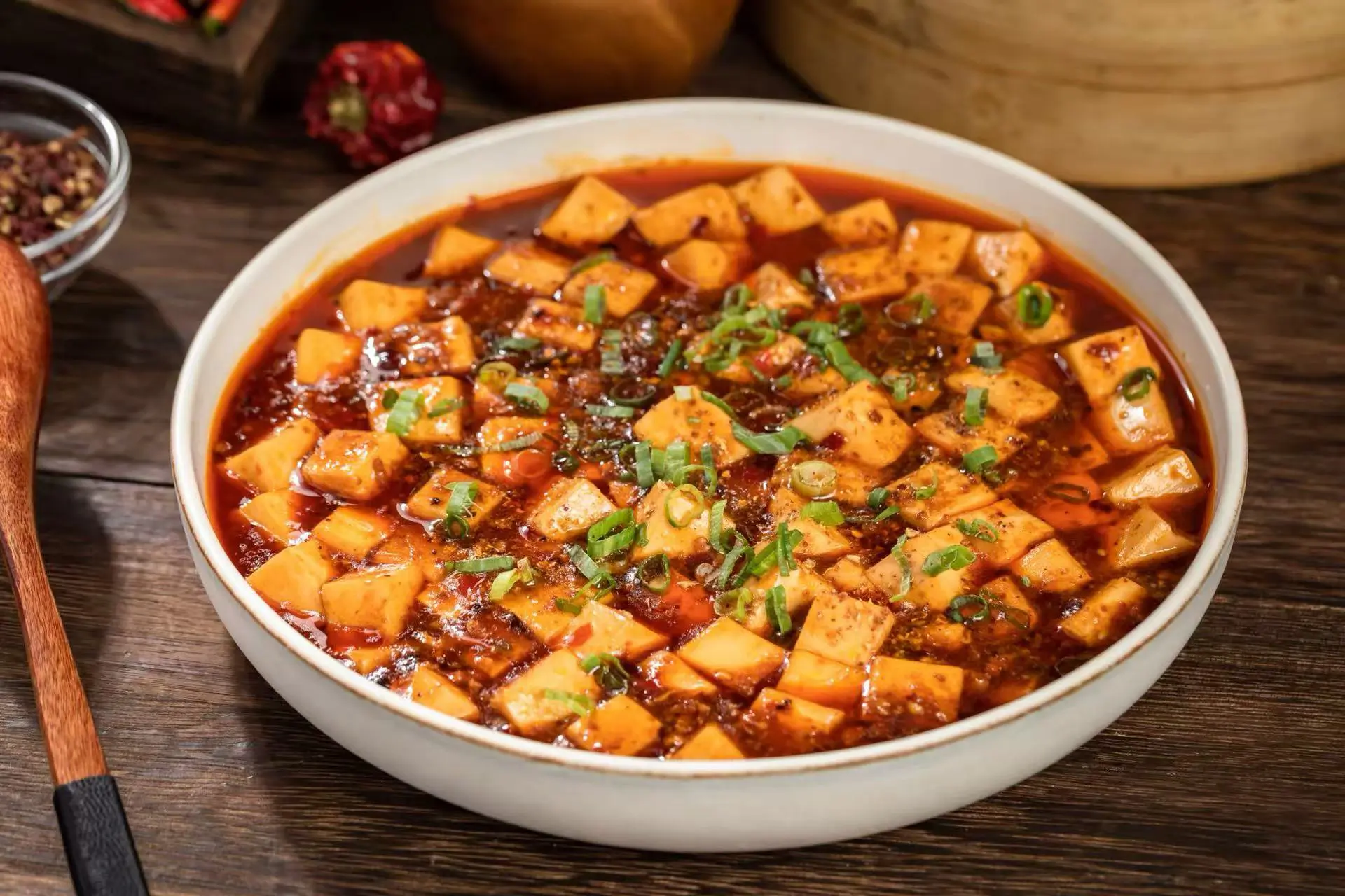 Mapo Tofu in a white bowl, tender tofu cubes in spicy red sauce, garnished with scallions at Spice Spirit JC, a Chinese restaurant in Jersey City